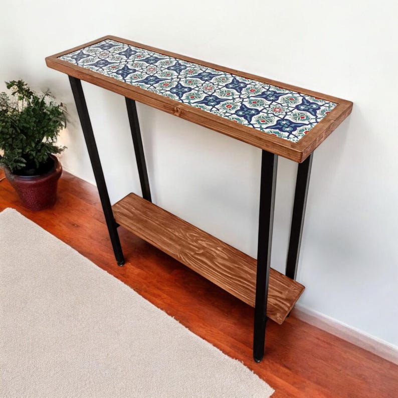 May include: A rectangular console table with a wooden frame and a patterned tile top. The table has black metal legs and a lower shelf. The tile design features blue, red, and green floral patterns.