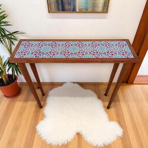 May include: A wooden console table with a geometric patterned tile top. The table has a dark brown wood finish and two slender legs.