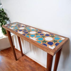 May include: A wooden console table with a geometric tile top. The tile features a repeating pattern of blue, green, yellow, and white stars. The table has two legs and is made of natural wood.