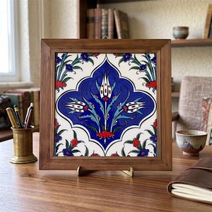 May include: A square ceramic tile featuring a central blue medallion with white and red tulip motifs, framed in a dark wood border. The tile displays intricate floral patterns in shades of blue, red, and green against a white background.