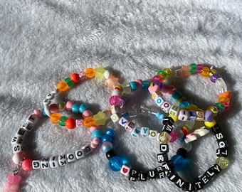 May include: Five colourful beaded bracelets with letter beads spelling out the words "Sweet Dreams", "Looking", "Over You", "Definitely", and "Lost" with a pink gummy bear charm on the "Sweet Dreams" bracelet.