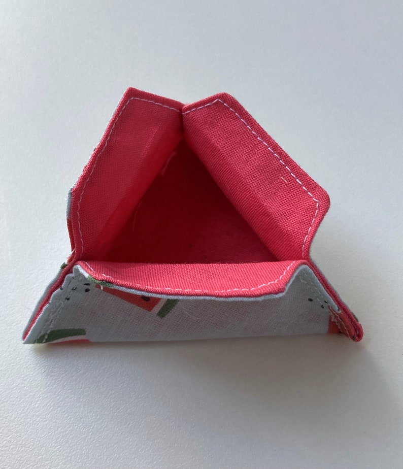 K&ouml;nnte beinhalten: Ein dreieckiger Stoffaufbewahrungskorb mit rosa Futter und einem Wassermelonenmuster auf der Au&szlig;enseite.