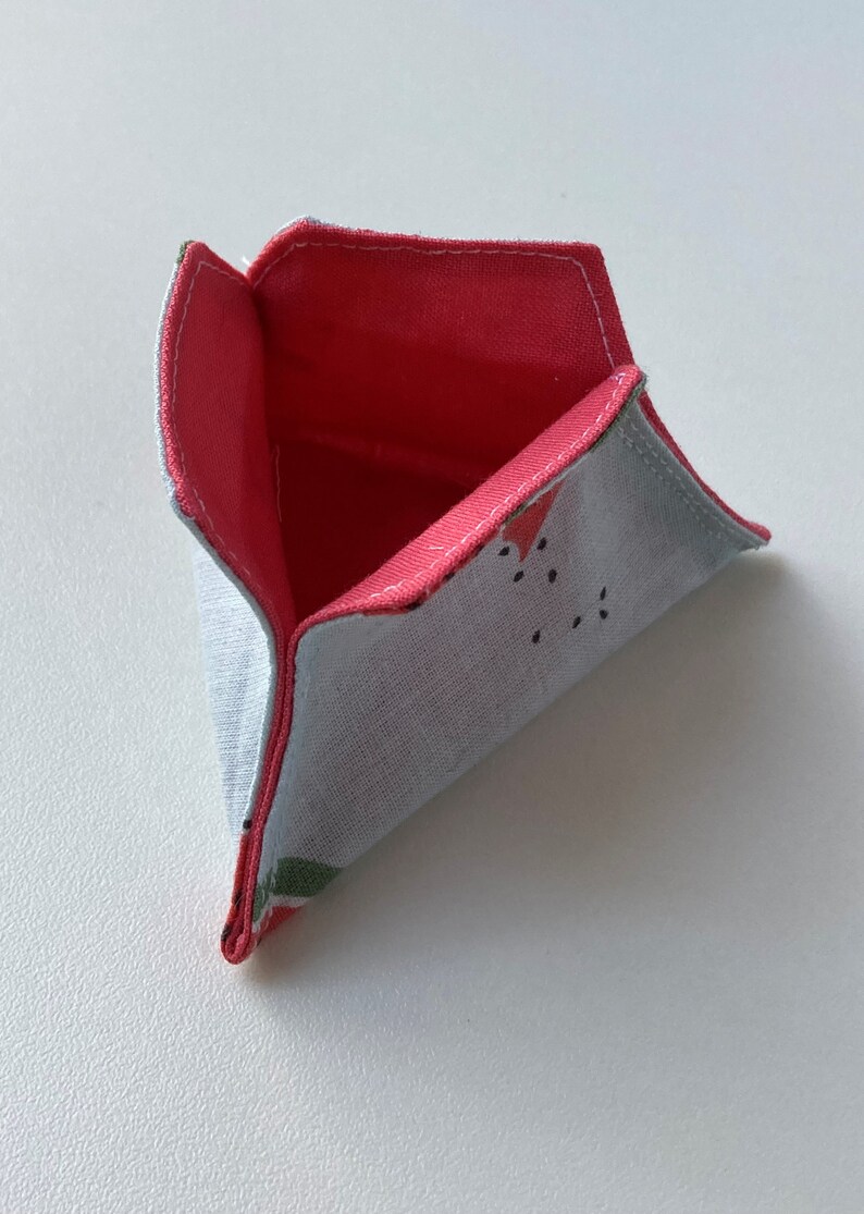 K&ouml;nnte beinhalten: Eine kleine dreieckige Stofftasche mit rotem Futter und einem Wassermelonenmuster auf der Au&szlig;enseite.