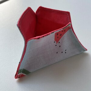 K&ouml;nnte beinhalten: Eine kleine, dreieckige Stofftasche mit Wassermelonenmuster. Die Tasche ist aufgeklappt und zeigt ein rosafarbenes Futter.