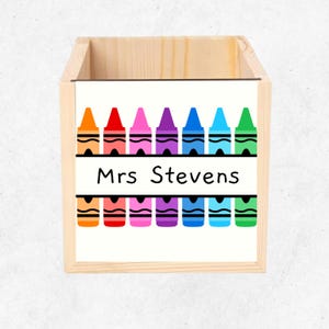May include: Wooden storage box with a white label featuring a row of colourful crayons and the text "Mrs. Stevens".