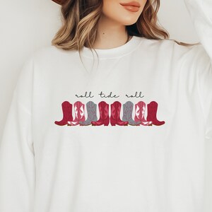 May include: White sweatshirt with a red and gray cowboy boot design and the text "roll tide roll" in black.