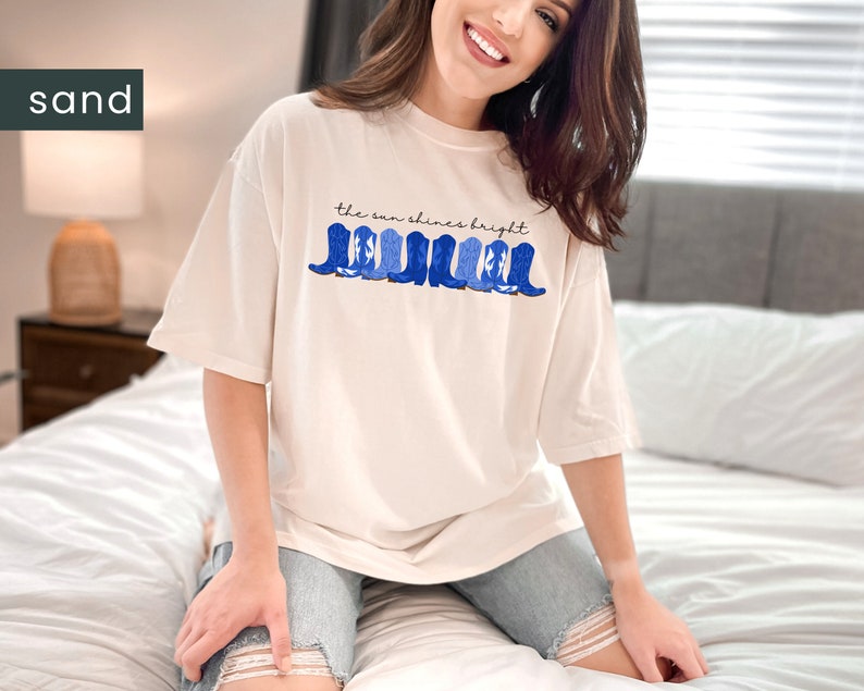 May include: A white t-shirt with a blue and white graphic of cowboy boots and the text "the sun shines bright".