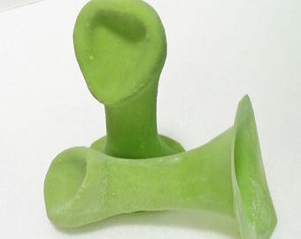May include: Two light green, abstract sculptures. One is upright, resembling a stylized head with a long neck. The other is horizontal, with a flared opening. The sculptures have a textured surface and are set against a white background.