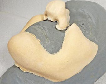May include: A prosthetic nose and cheek piece in a light beige color, designed to be applied to a gray surface. The prosthetic has a textured surface and is likely made of foam or a similar material.