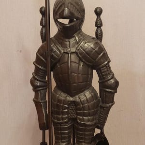 May include: A cast iron knight figure, holding a polearm and a shovel. The knight is clad in detailed armour and stands on a base. The figure is dark brown and is likely used as a fireplace tool holder.