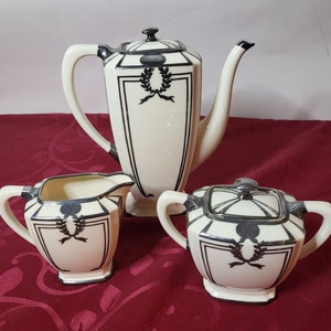 May include: A black and white porcelain tea set with a geometric design. The teapot, creamer, and sugar bowl have a silver trim and a black and white geometric design.