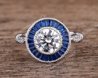 May include: A silver ring with a round, clear center stone surrounded by a halo of blue sapphires. The ring has a delicate band with small accent stones.
