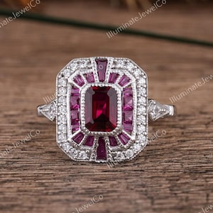 May include: A silver ring with a large, emerald-cut ruby surrounded by smaller rubies and diamonds. The ring has a vintage-inspired design.