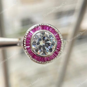 May include: A silver ring with a large round clear center stone surrounded by a halo of pink baguette stones.