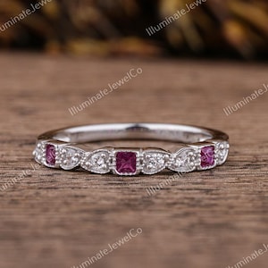 Puede incluir: Una banda plateada delicada con una fila de pequeños diamantes y tres piedras preciosas cuadradas de color rosa.