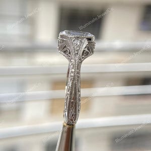 May include: A silver engagement ring with a large oval-shaped diamond set in a filigree design. The band is also decorated with intricate filigree details.