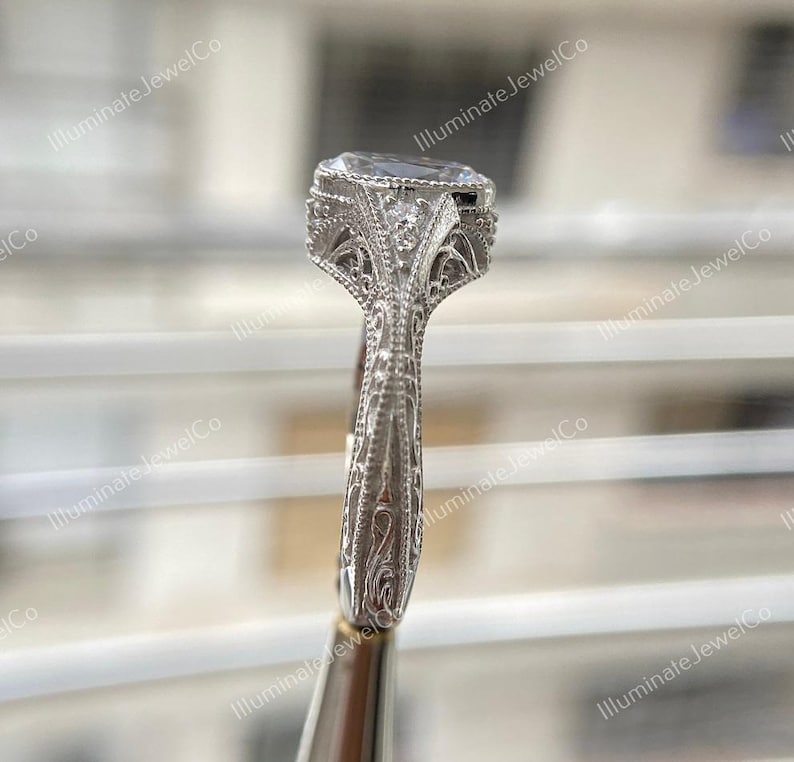 May include: A silver engagement ring with a large oval-shaped diamond set in a filigree design. The band is also decorated with intricate filigree details.