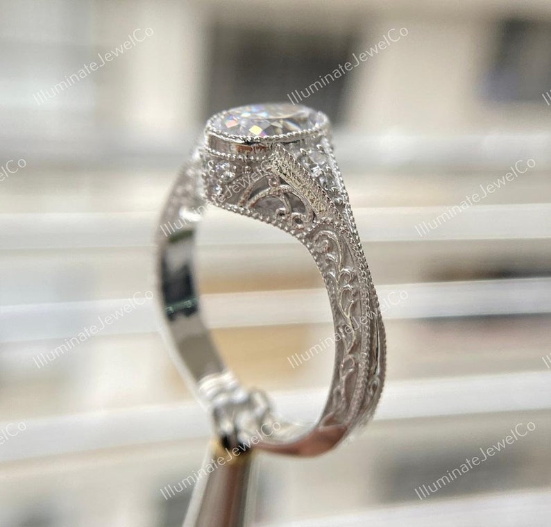 May include: A silver engagement ring with a round, clear center stone and intricate floral detailing on the band.