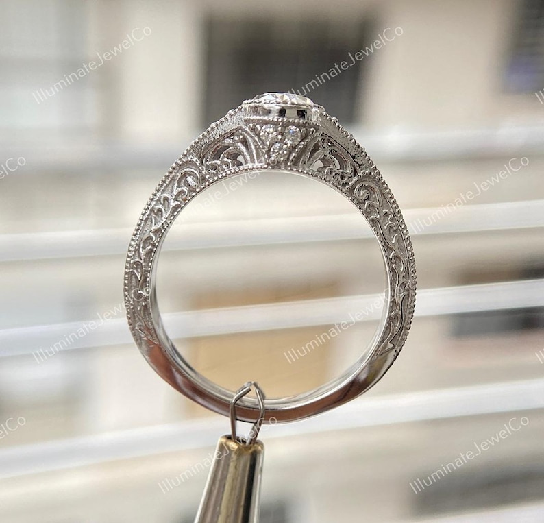 May include: A silver engagement ring with a round center stone and intricate filigree detailing on the band.