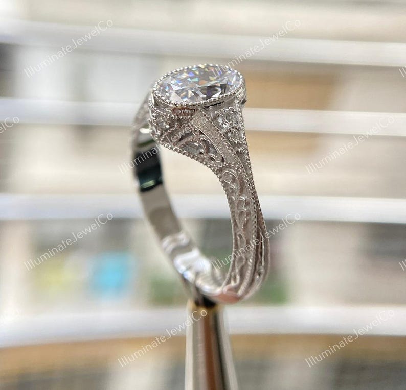 May include: A silver engagement ring with a large oval-shaped diamond set in a filigree design. The ring is on a display stand.