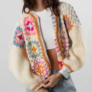Puede incluir: Cárdigan de crochet color crema con patrones cuadrados coloridos. El suéter abierto presenta una mezcla de cuadrados rosas, azules, naranjas y amarillos, con mangas y ribetes color crema. Una prenda única hecha a mano.
