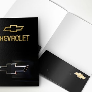 May include: A black folder with a gold Chevrolet logo and the word "CHEVROLET" printed in gold. The folder is open to reveal a white interior.