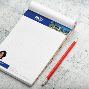 Puede incluir: Un bloc de notas blanco con detalles azules y el logotipo "exp realty", una foto de casas y un retrato de una mujer. Un lápiz rojo descansa junto al bloc de notas sobre una superficie texturizada.