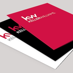 May include: Three layered business documents in red, black, and white. The top red document displays the white text "kw KELLER WILLIAMS." The black document is beneath the red, and the white document is at the bottom. The documents are slightly angled.