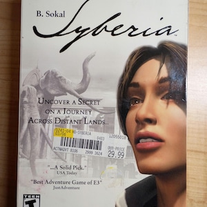 May include: Syberia video game box featuring a woman's face and an illustration of elephants. The box has the game title in a stylized font and text that reads "Uncover a Secret on a Journey Across Distant Lands..." The Adventure Company logo is visible.