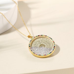May include: A gold-colored pendant necklace with a round, detailed pendant. The pendant has a gold frame with a ring of colorful gemstones. The pendant's center features a detailed design with a silver and gold color scheme. The necklace chain is also gold.