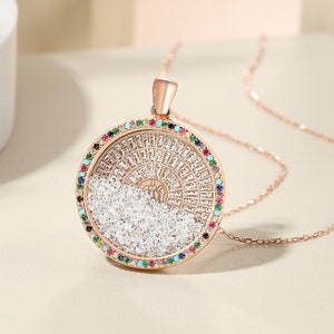 May include: Rose gold pendant necklace with a circular design. The pendant features a ring of colorful gemstones surrounding a detailed central design with clear crystals. The necklace is displayed on a neutral background.