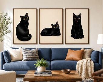 May include: A set of three framed wall art prints featuring black cats with yellow eyes against a cream background. The left print shows a sitting cat, the center print shows a reclining cat, and the right print shows a cat sitting with its tongue out.