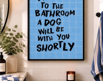 May include: A rectangular wall art print in a black frame featuring a light blue grid background with the black text: WELCOME TO THE BATHROOM A DOG WILL BE WITH YOU SHORTLY. The design mimics a tiled wall surface with bold, hand-lettered style typography.
