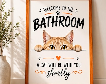 May include: Framed wall art with a brown wooden frame. The artwork features a tabby cat peeking over a black line, with the words "WELCOME TO THE BATHROOM" and "A CAT WILL BE WITH YOU shortly" in black and orange.
