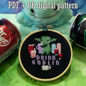 May include: A cross-stitch embroidery in a wooden hoop features a green creature with the text "DRINK GOBLIN". The image includes a Dr. Pepper can, a green soda can, and a plush toy. The text "PDF + PK digital pattern" is at the top.