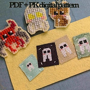 May include: A selection of cross-stitch patterns, featuring a red devil, a grey monster, a brown bear, and tooth designs. The text "PDF + PK digital pattern" is at the top. The items are on a yellow felt surface.