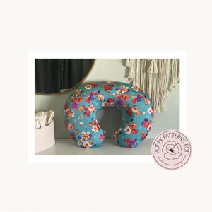 The back view of the handmade nursing pillow cover designed by PoppyPatternsPDF and made with a blue floral print fabric. Pillow is laying upright on a white dresser. PoppyPatternsPDF Logo is featured in the bottom right corner.
