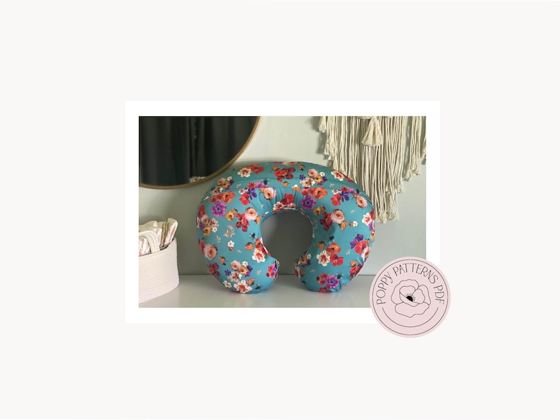 The back view of the handmade nursing pillow cover designed by PoppyPatternsPDF and made with a blue floral print fabric. Pillow is laying upright on a white dresser. PoppyPatternsPDF Logo is featured in the bottom right corner.
