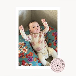 An image of the handmade nursing pillow cover with being used by a baby with their arms raised in the air. PoppyPatternsPDF Logo is featured in the bottom right corner.