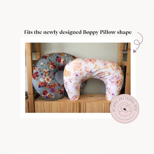 May include: Two Boppy nursing pillows with floral patterns. One pillow is blue with red, orange, and yellow flowers. The other is white with pink and orange flowers. The text "Fits the newly designed Boppy Pillow shape" is above the pillows.