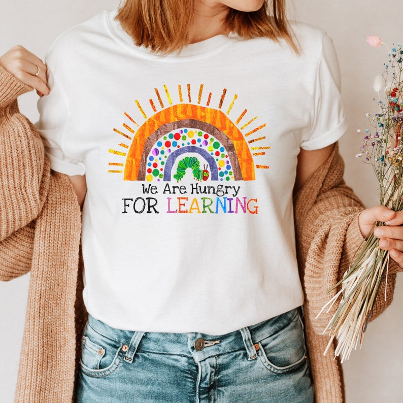 Peut inclure: T-shirt blanc avec un arc-en-ciel et un graphique de chenille. Le texte "We Are Hungry For Learning" est imprim&eacute; sous le graphique.