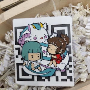 May include: Enamel pin featuring a cartoon illustration of two characters and a white creature with blue and purple accents. The pin is set against a black and white patterned background, inside a wooden box with paper filler.