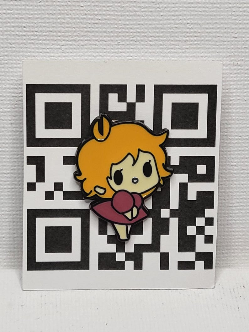 May include: A colourful enamel pin depicting a cartoon girl with orange hair and a pink dress. The pin is set against a white background with a black and white QR code design. A cute accessory.