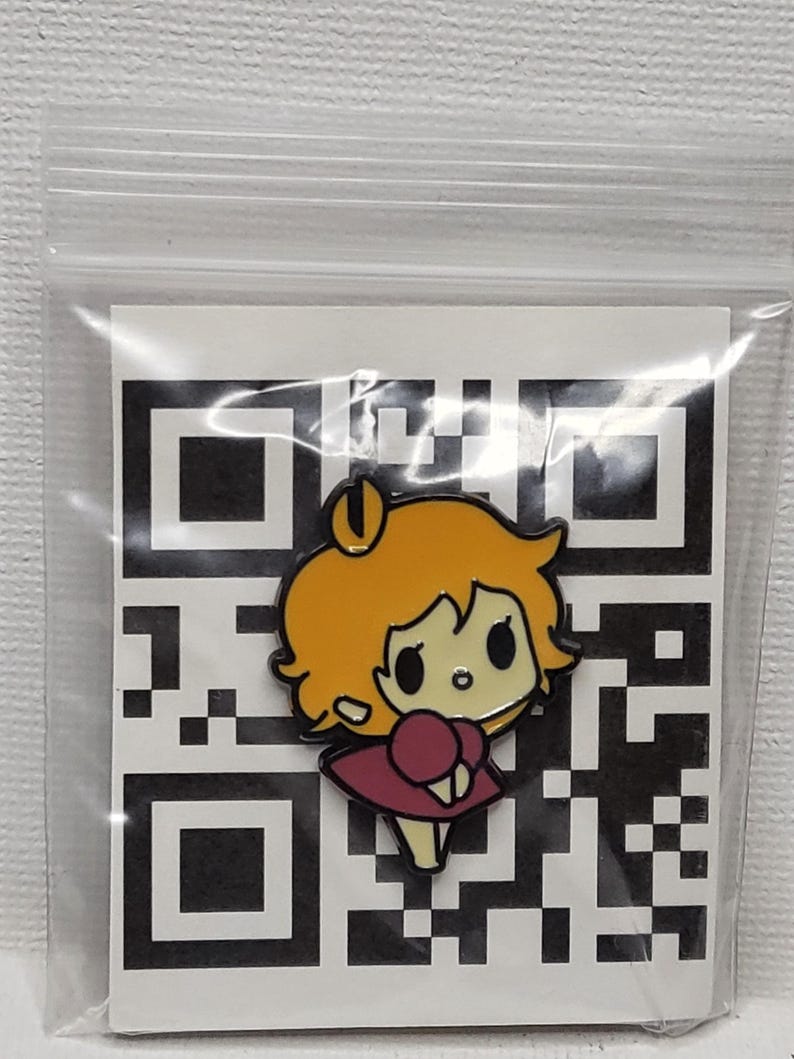 May include: A cartoon character enamel pin with orange hair and a maroon dress. The pin is set against a black and white QR code background, enclosed in a clear plastic bag.