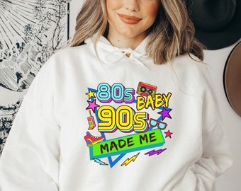 May include: White hoodie with a colorful graphic design. The design features the text "80s BABY 90s MADE ME" in yellow, blue, and green, along with images of a cassette tape, roller skate, and stars. A fun, retro-themed sweatshirt.