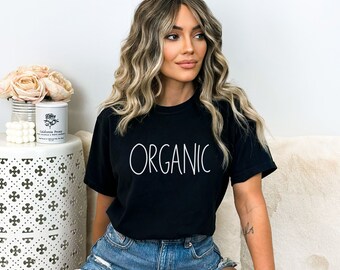 May include: A woman wearing a black t-shirt with the word "ORGANIC" printed in white on the front. She is wearing denim shorts and has long blonde hair.