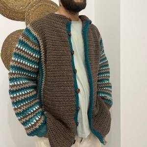 May include: A brown crocheted cardigan with teal and white stripes on the sleeves. The cardigan has a button closure and a hood.