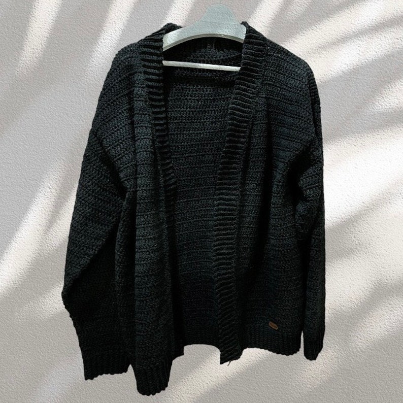 May include: A black knitted cardigan with a long sleeve and a v-neck. The cardigan is open in the front and has a ribbed texture.