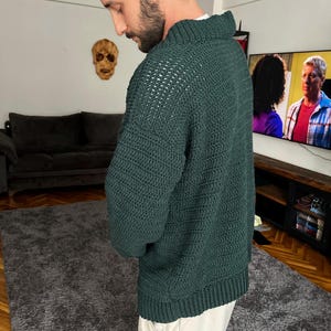 May include: A dark green knitted sweater with a textured pattern. The sweater has a high neckline and long sleeves.