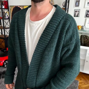 May include: A dark green knitted cardigan with a deep V-neck and long sleeves.